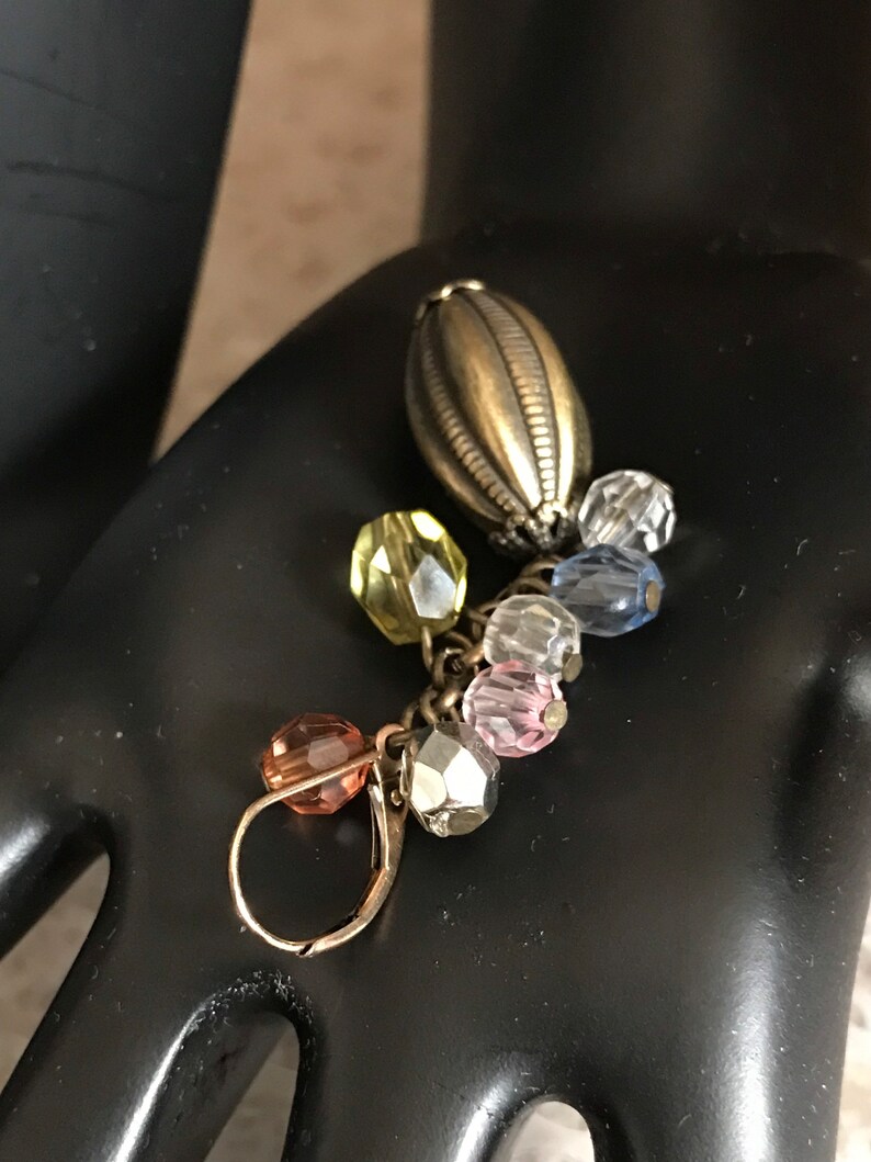Puede incluir: Un pendiente de plata con un dije en forma de l&aacute;grima y un racimo de cuentas de vidrio de colores en tonos rosa, azul, amarillo y transparente.