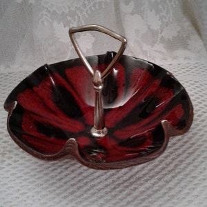 May include: A red and black ceramic serving dish with a silver handle. The dish has a scalloped edge and a raised center.