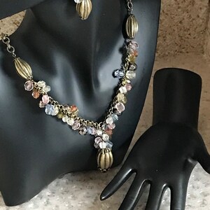 Puede incluir: Un collar de m&uacute;ltiples hilos y pendientes a juego con una cadena de bronce y cuentas de cristal de colores. El collar tiene un colgante en forma de l&aacute;grima con una tapa de bronce. Tambi&eacute;n se muestra un anillo a juego con una tapa de bronce y cuentas de cristal.