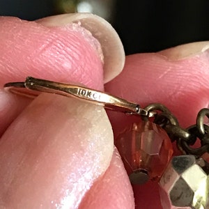 Puede incluir: Primer plano de un pendiente de oro con un sello de 10K. El pendiente tiene una peque&ntilde;a cuenta de vidrio rosa y una cuenta plateada.