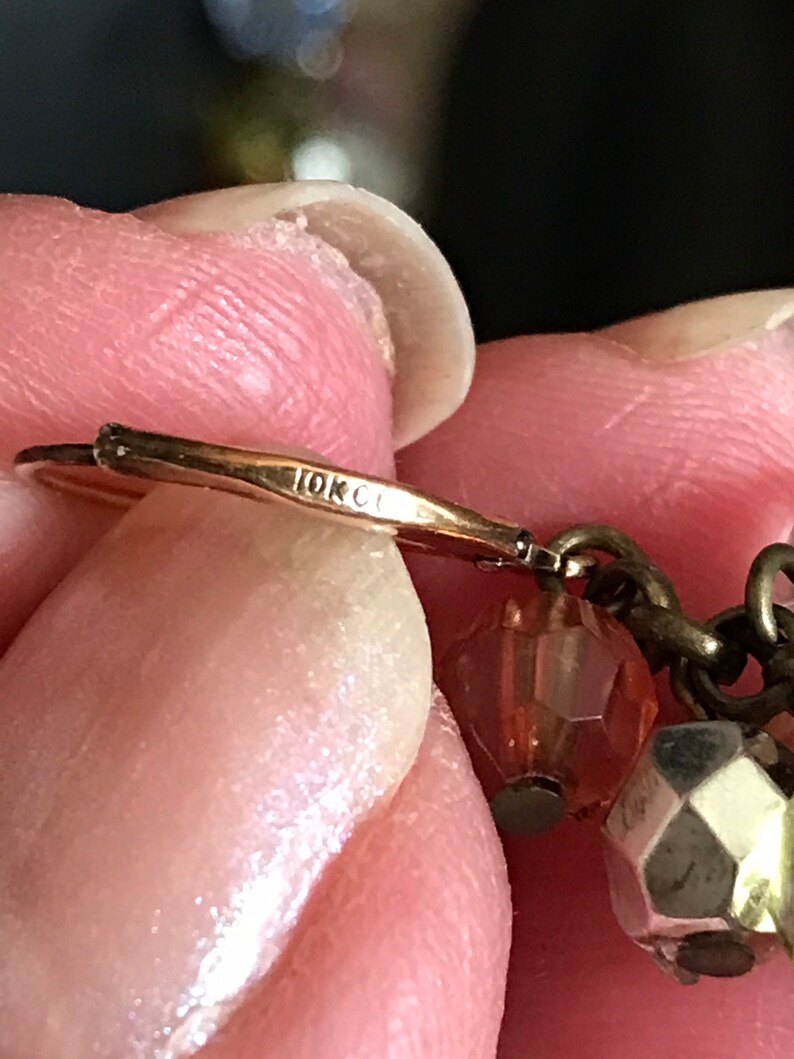 Puede incluir: Primer plano de un pendiente de oro con un sello de 10K. El pendiente tiene una peque&ntilde;a cuenta de vidrio rosa y una cuenta plateada.