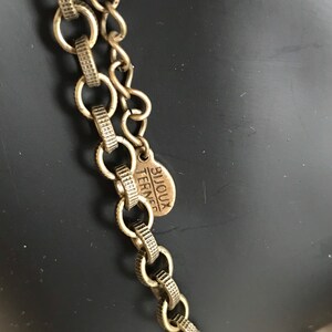 Puede incluir: Un collar de cadena dorada con una peque&ntilde;a etiqueta redonda que dice "Bijoux Terner".