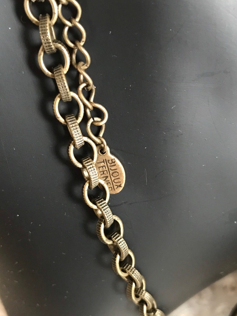 Puede incluir: Un collar de cadena dorada con una peque&ntilde;a etiqueta redonda que dice "Bijoux Terner".