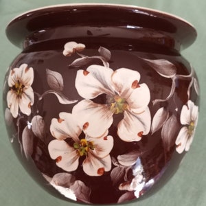 May include: A brown ceramic planter with white flowers painted on the side. The flowers have a light brown center and green leaves.