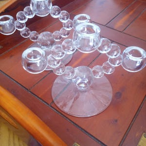 May include: A clear glass candle holder with a beaded design. The holder has five candle cups and a wide base.