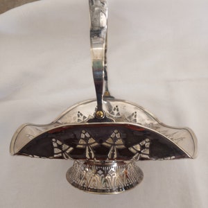 May include: A silver serving basket with an ornate design and a handle. The basket has a scalloped edge and a decorative base.