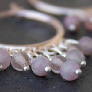 May include: Silver hoop earrings with a delicate chain and multiple light purple beads hanging from the bottom.