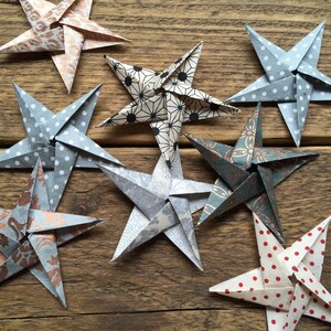May include: An assortment of handmade origami stars in various patterns and colors, including polka dots, floral designs, and geometric shapes. The stars are arranged on a rustic wooden surface, showcasing their intricate folds and textures.