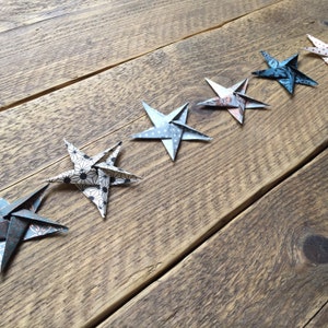 May include: A line of origami stars in various patterns and colors, including blue, white, and patterned paper, are arranged diagonally on a rustic wooden surface. The stars are folded with intricate detail, showcasing a handmade craft.