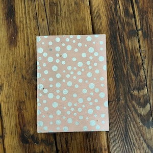 Puede incluir: Una libreta rosa con un patrón de lunares blancos. La libreta está hecha de papel reciclado y tiene una superficie texturizada.