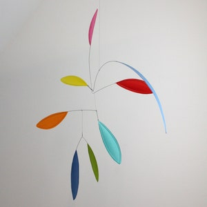 May include: A colorful mobile with seven leaves of different colors and shapes. The leaves are suspended from a central point and move freely in the air. The mobile is made of metal and fabric.