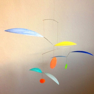 Può includere: Un mobile colorato con forme geometriche di carta e filo. Il mobile presenta forme di colore azzurro, giallo, arancione, verde e blu.