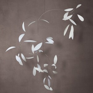 May include: A white mobile sculpture with multiple paper leaves hanging from thin wires. The leaves are suspended in a circular pattern, creating a sense of movement and balance.