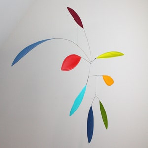 May include: A colorful mobile with seven hanging leaves in various colors, including red, blue, yellow, green, and turquoise. The leaves are suspended from a central point and move freely in the air.