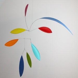 May include: A colorful mobile with seven hanging pieces in various shapes and sizes. The pieces are made of paper and are painted in different colors, including red, orange, yellow, green, blue, and turquoise. The mobile is suspended from the ceiling by a thin wire.