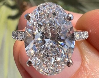 May include: A large oval-shaped diamond engagement ring with a halo setting. The ring is set in white gold and features a pave diamond band.