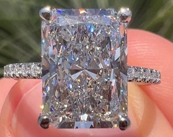 May include: A silver ring with a large, clear, rectangular-shaped diamond. The diamond has a lot of sparkle and is set in a prong setting. The band of the ring is thin and has small diamonds set in a pave setting.