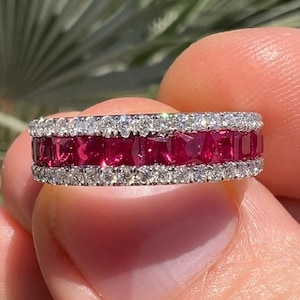 May include: A gold band ring with a row of red ruby stones and two rows of smaller diamonds.
