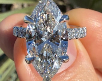 May include: A silver ring with a large, clear marquise-shaped diamond set in a prong setting. The band is adorned with smaller diamonds.