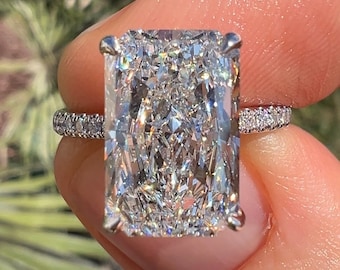 Könnte beinhalten: Ein großer, klarer, rechteckiger Diamantring mit einem silbernen Band. Das Band ist mit kleineren Diamanten besetzt.