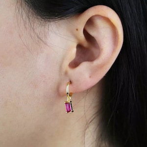 Op de afbeelding: Gouden creolen met een hangende roze rechthoekige edelsteen.