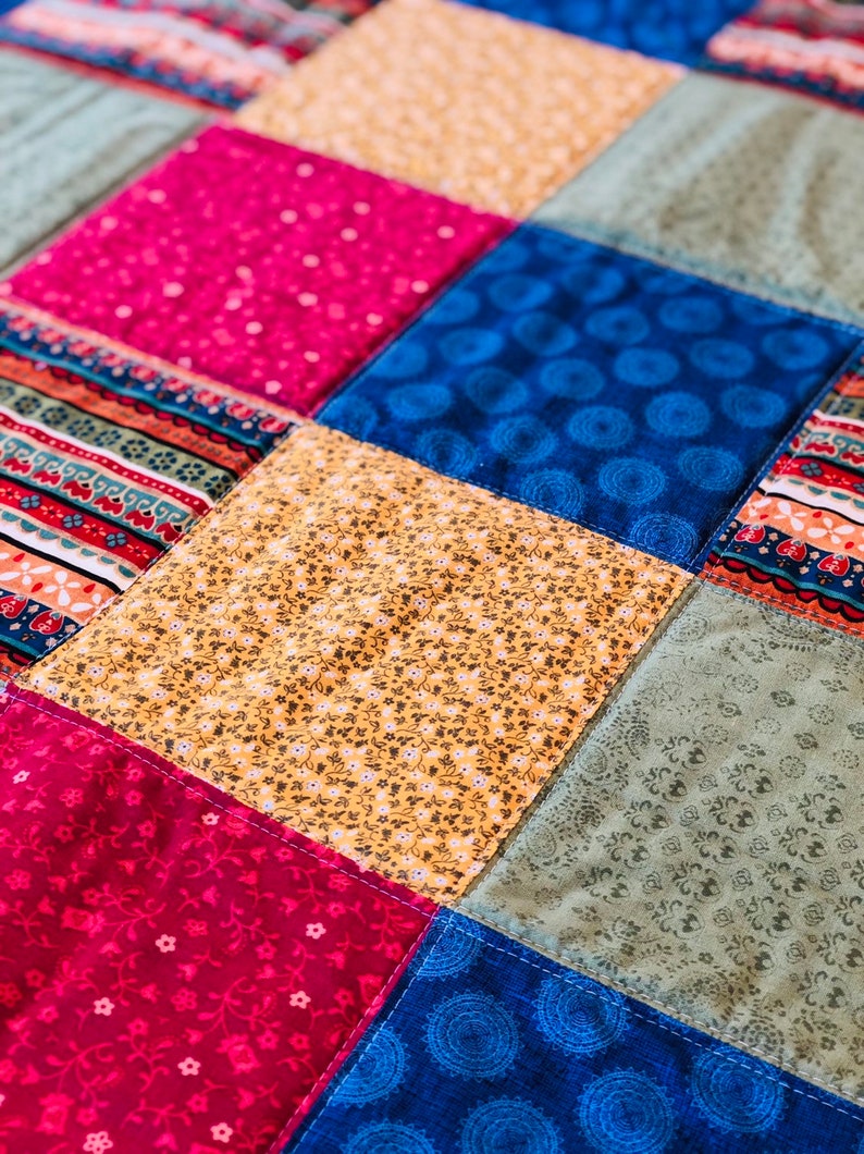 Op de afbeelding: Een patchworkdeken met vierkanten in verschillende kleuren en patronen, waaronder roze, blauw, geel en groen.