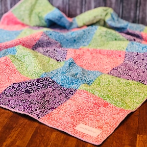 May include: A patchwork quilt with a floral pattern in shades of pink, green, purple, and blue. The quilt is folded and has a tag that says "pretty things".