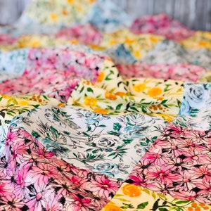 Puede incluir: Una colcha de retazos con una variedad de patrones florales en tonos de rosa, azul, amarillo y blanco. La colcha está hecha de diferentes telas y texturas, creando un diseño único e interesante.