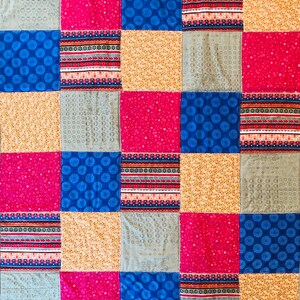 Op de afbeelding: Een patchworkdeken met een verscheidenheid aan kleurrijke stoffen. De deken is gemaakt van vierkanten in verschillende kleuren en patronen, waaronder blauw, rood, geel en grijs. De deken is een geweldige manier om elke kamer een vleugje kleur en persoonlijkheid te geven.