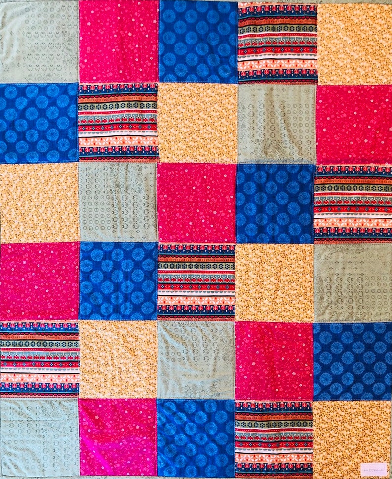 Op de afbeelding: Een patchworkdeken met een verscheidenheid aan kleurrijke stoffen. De deken is gemaakt van vierkanten in verschillende kleuren en patronen, waaronder blauw, rood, geel en grijs. De deken is een geweldige manier om elke kamer een vleugje kleur en persoonlijkheid te geven.