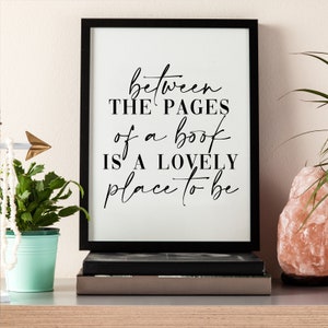 May include: Black and white framed print with the text "between the pages of a book is a lovely place to be" on a white background.