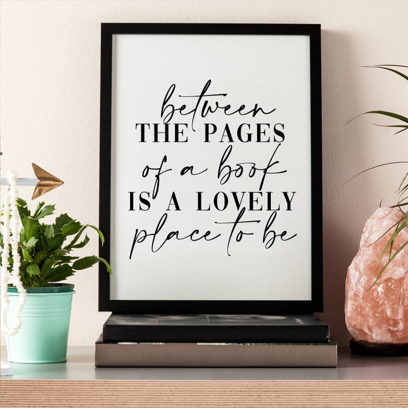 May include: Black and white framed print with the text "between the pages of a book is a lovely place to be" on a white background.