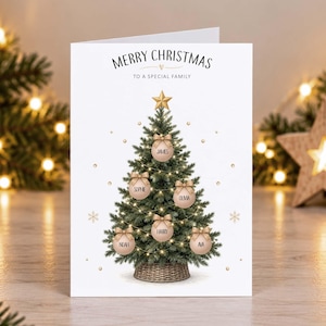 May include: A white Christmas greeting card featuring a green pine tree topped with a gold star. The tree is decorated with string lights and five pale pink ornaments, each labeled with the names James, Sophie, Olivia, Harry, and Noah.