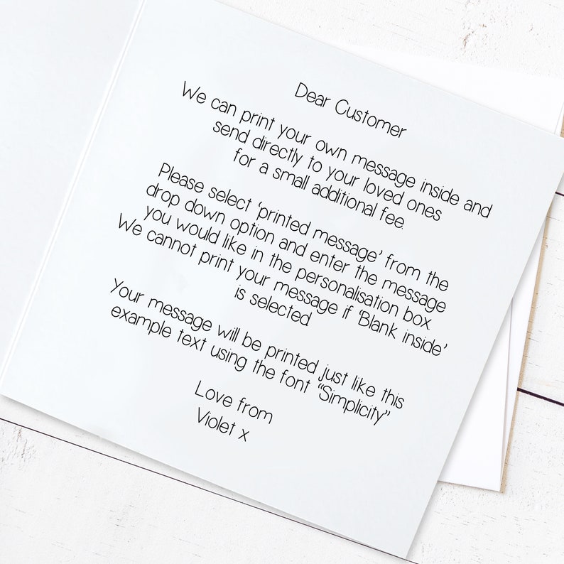May include: A white card with black text explaining how to personalize a message for a loved one. The text reads: "Dear Customer, We can print your own message inside and send directly to your loved ones for a small additional fee. Please select 'printed message' from the drop down option and enter the message you would like in the personalisation box. We cannot print your message if 'Blank inside' is selected. Your message will be printed just like this example text using the font "Simplicity". Love from Violet x"