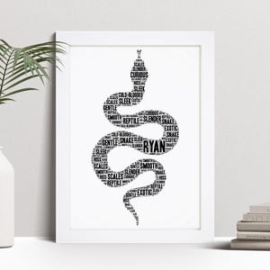 May include: A framed black and white art print depicting a snake formed from words such as "scales," "sleek," and "exotic." The name "Ryan" is integrated into the snake's design. The print is displayed on a white wall.