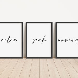 May include: Three black framed prints with white backgrounds and black calligraphy. The prints read "relax", "soak", and "unwind".
