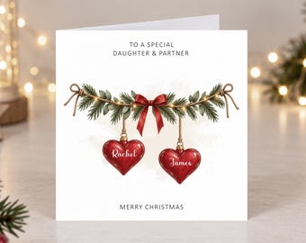 May include: A white square Christmas greeting card featuring the text TO A SPECIAL DAUGHTER & PARTNER and MERRY CHRISTMAS. The design shows a green pine garland with a red bow and two red heart-shaped ornaments labelled Rachel and James.