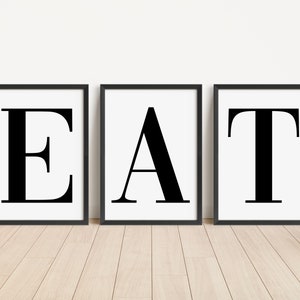 May include: Three black framed prints with white backgrounds, each featuring a large black letter, spelling out the word "EAT".