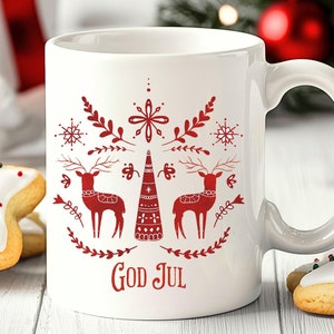 May include: White ceramic mug with a red and white Christmas design. The design features a stylized Christmas tree, two reindeer, and snowflakes. The text "God Jul" is printed in red at the bottom of the mug.