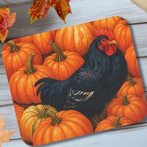 Op de afbeelding: Een vierkant decoratief dienblad met een zwarte haan met een rode kam en lellen, omringd door oranje pompoenen. De pompoenen hebben groene stelen. Herfstbladeren zijn rond de lade verspreid.