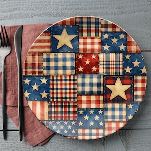 Puede incluir: Un plato decorativo con un diseño de patchwork con patrones rojos, blancos y azules, incluyendo estrellas y rayas. El plato está acompañado de un tenedor, un cuchillo y una servilleta roja, sobre una superficie de madera gris.