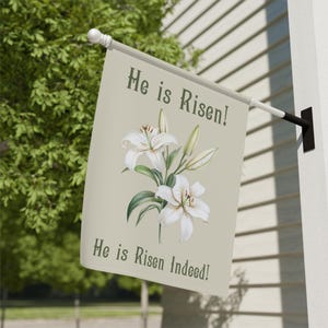以下が含まれることがあります： 白いユリと「He is Risen!」「He is Risen Indeed!」の文字が書かれたベージュの布製のガーデンフラッグ