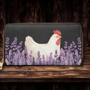 Könnte beinhalten: Schwarze Geldbörse mit einem weißen Hühnerdesign. Das Huhn hat einen roten Kamm und Schnabel, vor einem Hintergrund aus lila Lavendel. Die Geldbörse hat einen goldenen Reißverschluss und ist aus strukturiertem Material.