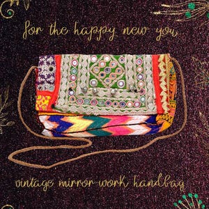Puede incluir: Un bolso vintage de espejo de trabajo colorido con una correa marrón. El bolso está decorado con bordados y espejos coloridos. El texto "for the happy new you" y "vintage mirror-work handbag" está escrito en letras doradas sobre un fondo oscuro brillante.