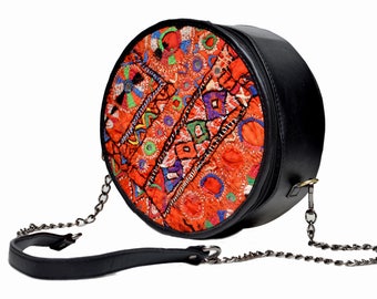 May include: A round black leather crossbody bag with a colorful embroidered flap. The bag has a chain strap and a leather shoulder strap.