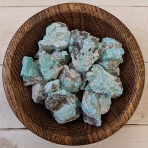 May include: A wooden bowl filled with rough, teal green and gray amazonite crystals.