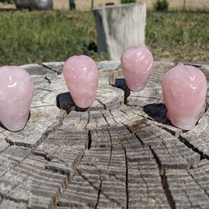 Puede incluir: Cuatro tallas de cabeza de extraterrestre de cuarzo rosa sobre una superficie de madera.