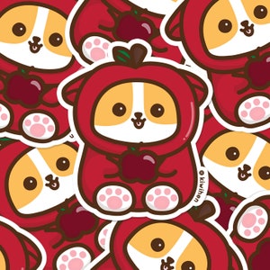 May include: A repeating pattern of cartoon corgis dressed as apples. Each corgi is wearing a red apple costume and holding a red apple. The corgis have brown eyes, tan and white fur, and pink paw pads. The background is red.