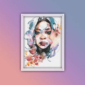 Op de afbeelding: Een aquarel schilderij van een vrouwen gezicht met kleurrijke verfspatten eromheen. De vrouw heeft donker haar en bruine ogen. Het schilderij is gemaakt in een zachte, dromerige stijl.