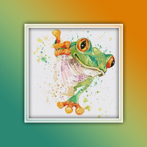 Könnte beinhalten: Ein grüner und orangefarbener Frosch mit großen Augen und einem breiten Lächeln, im Aquarell-Stil mit Farbspritzern gemalt.